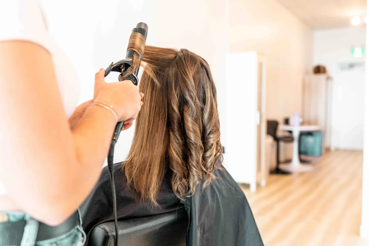A stylist curling and finishing a fresh blow-dry inside the bright Aura Hair Studio salon